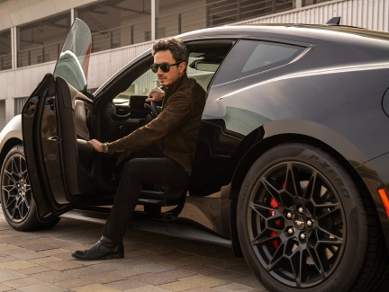 A stylish person in sunglasses getting into a black Ford Mustang with the door open, emphasising the car's customizable features and personal style.