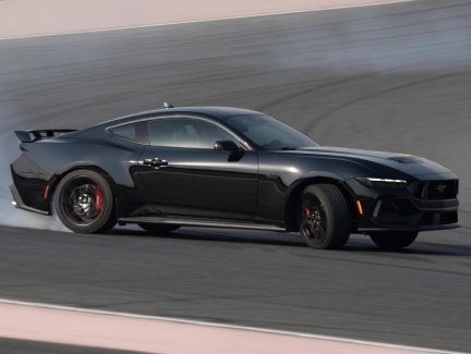 Rear three-quarter view of a gray Mustang driving around a race track, highlighting its sleek profile and sporty rear.