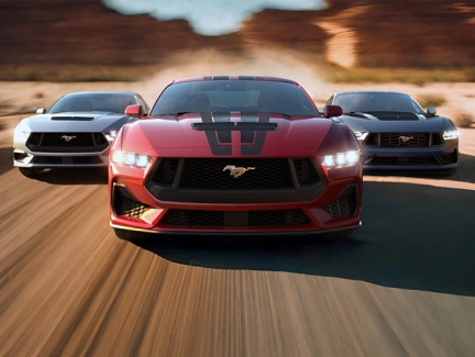 Three Ford Mustangs in different colors (red, silver, blue) driving on a desert road, showcasing available paint options.