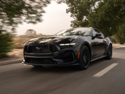 Front view of a black Ford Mustang driving aloing a road.
